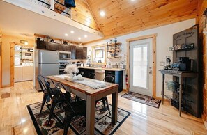 Une cuisine moderne avec des poutres en bois au plafond, un coin repas avec une table et des chaises, et un espace dédié à la préparation du café.