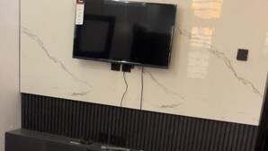 Un salon moderne avec un téléviseur à écran plat fixé sur un mur en marbre, une console en bois foncé dotée de tiroirs et un sol carrelé de couleur grise.
