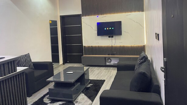Un salon moderne avec un téléviseur à écran plat fixé à un mur en marbre, un canapé noir, une table basse et un tapis noir et blanc.