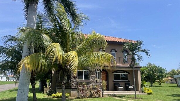 A two-story house with a stone facade, a red-tiled roof, and a well-maintained lawn with palm trees. - Casa Inge: 3BR Golf-Front Villa at Gran Pacifica Resort. Pet Friendly! (Gran Pacifica Resort)