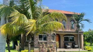 A two-story house with a stone facade, a red-tiled roof, and a well-maintained lawn with palm trees. - Casa Inge: 3BR Golf-Front Villa at Gran Pacifica Resort. Pet Friendly! (Gran Pacifica Resort)
