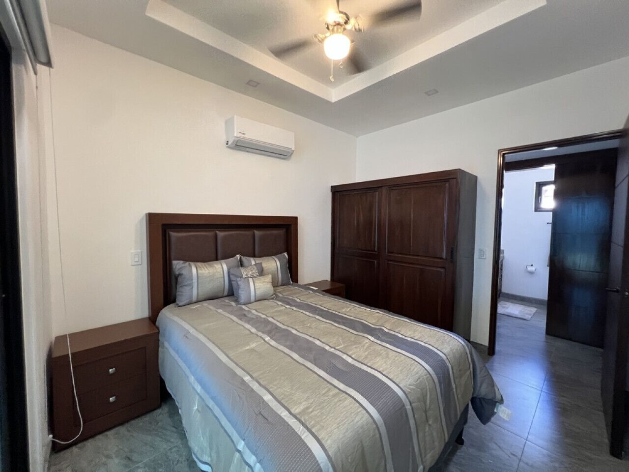 Un dormitori amb llit, armari de fusta, tauleta de nit i ventilador de sostre.