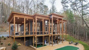 A two-story wooden cabin with a deck, outdoor seating, and a green artificial turf area. - New Luxe at Laurel - Putting Green in Blue Ridge (Blue Ridge)
