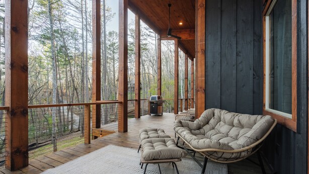 A wooden deck with a rocking chair and ottoman, large windows, and a view of the forest. - New Luxe at Laurel - Putting Green in Blue Ridge (Blue Ridge)
