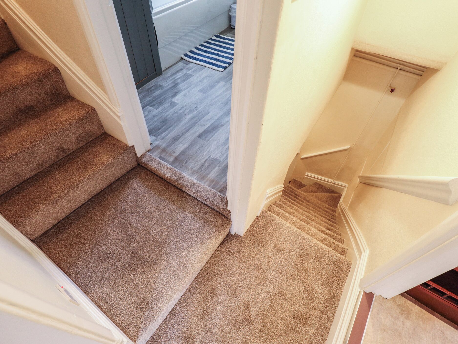 A carpeted staircase with a handrail and a landing area with a striped rug.