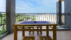 Un balcone con tavolo e panche in legno, ringhiera metallica e vista su strada e vegetazione.