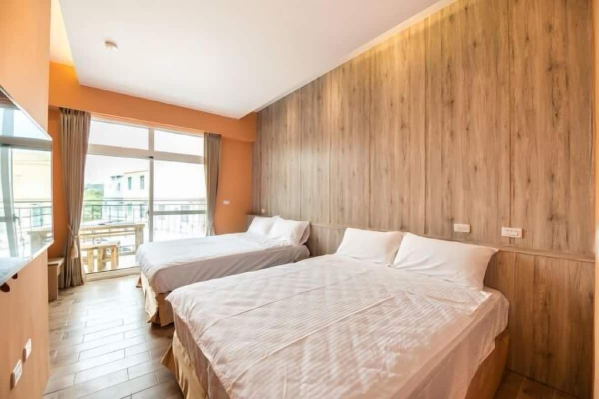 A hotel room with two beds, wooden paneling on one wall, and a balcony with a view.