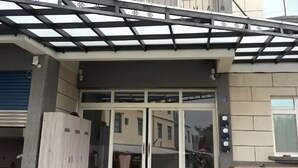 L'ingresso di un edificio con una porta in vetro, una panca in legno e un pergolato in metallo.