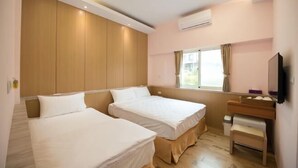Camera d'albergo con due letti singoli, una testiera in legno, una scrivania con una sedia, una finestra con tende e un condizionatore d'aria.