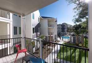 A balcony with a red chair, a blue chair, and a small pool area with palm trees. - First Floor Modern 3 Bedroom Condo in Beautiful NMB (North Myrtle Beach)