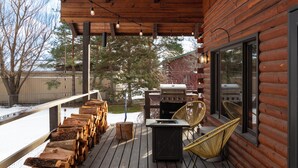 Un patio in legno con una griglia, sedie e legna impilata.