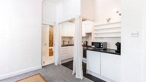 A modern kitchen with white cabinetry, a black countertop, and a microwave. - Elegant Knightsbridge Flat Near Harrods (London)