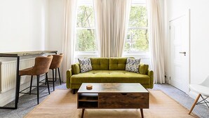 A room with a green sofa, two bar stools, a wooden coffee table, and a radiator. - Elegant Knightsbridge Flat Near Harrods (London)