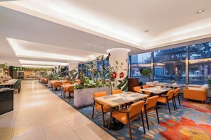 Un hall d’hôtel moderne doté d’un long comptoir d’accueil, de plusieurs espaces salon et de grandes fenêtres offrant une vue sur la ville.