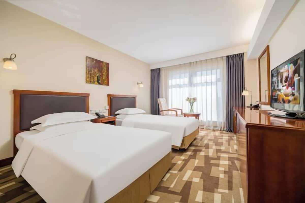 Habitación de hotel con dos camas, un escritorio, una silla, un televisor y una ventana con cortinas.