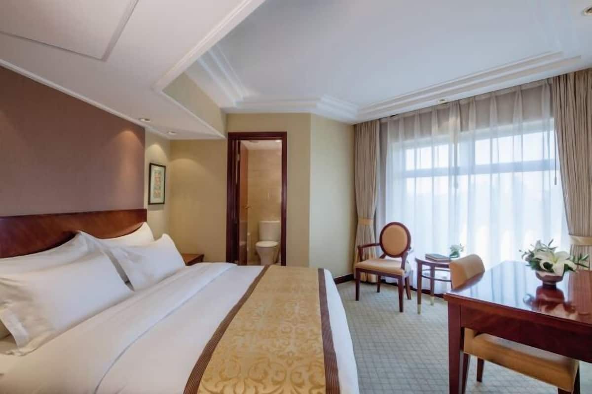 Habitación de hotel con una cama grande, un escritorio y una silla. Hay una puerta que da al baño.