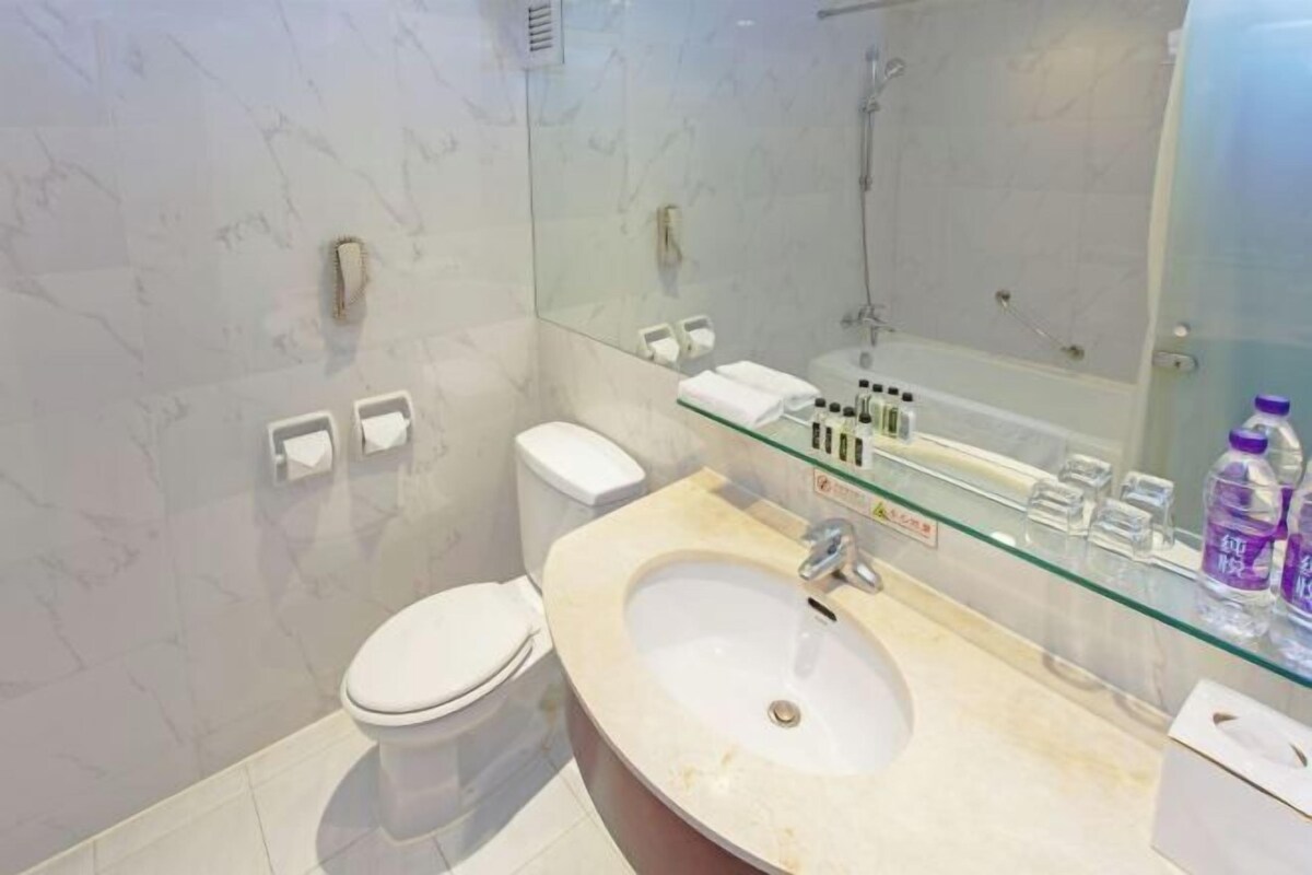 A modern bathroom with a glass shower enclosure, a marble-tiled wall, a white toilet, and a vanity with a glass shelf holding toiletries.