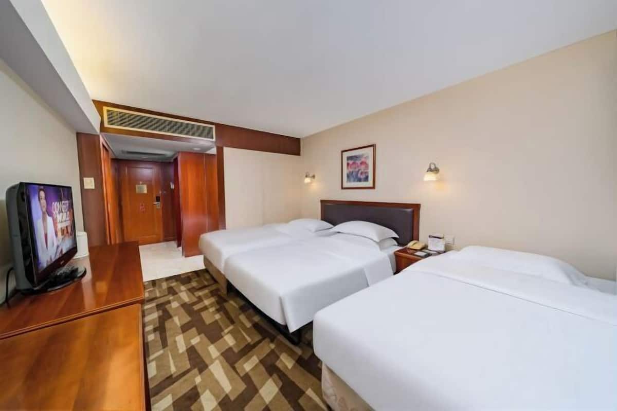 Habitación de hotel con dos camas, televisor, escritorio y puerta que da a un pasillo.