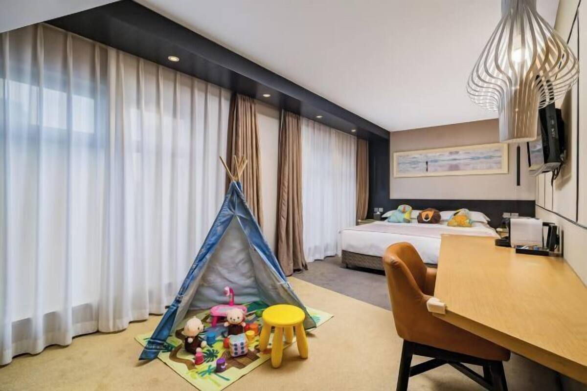Habitación de hotel con cama, escritorio, silla, mesita pequeña, una tienda de campaña infantil y una lámpara.