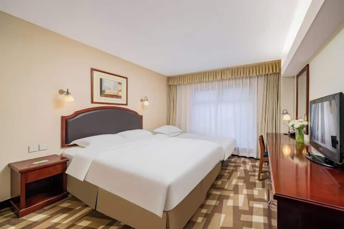 Una habitación de hotel con una cama grande, televisión, escritorio y ventana con cortinas.