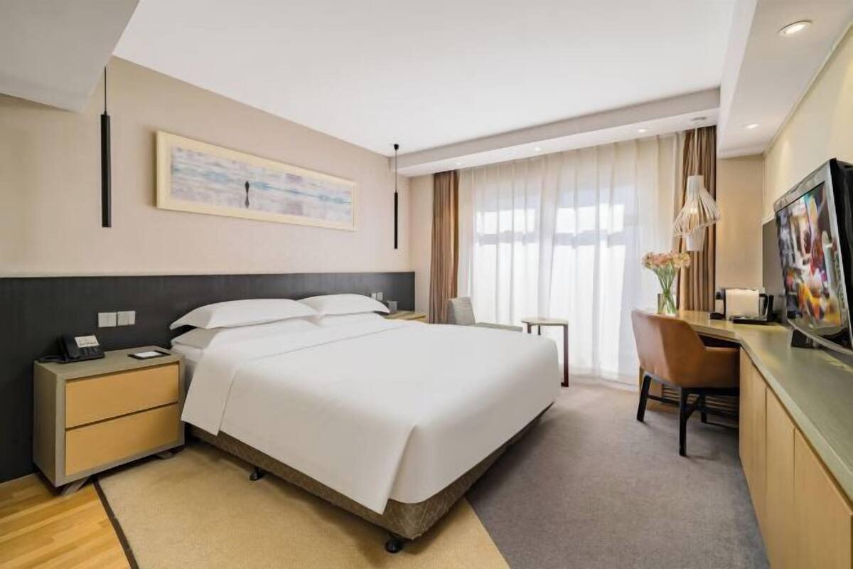 Habitación de hotel con una cama grande, mesitas de noche, un escritorio con silla, televisor y ventana con cortinas.