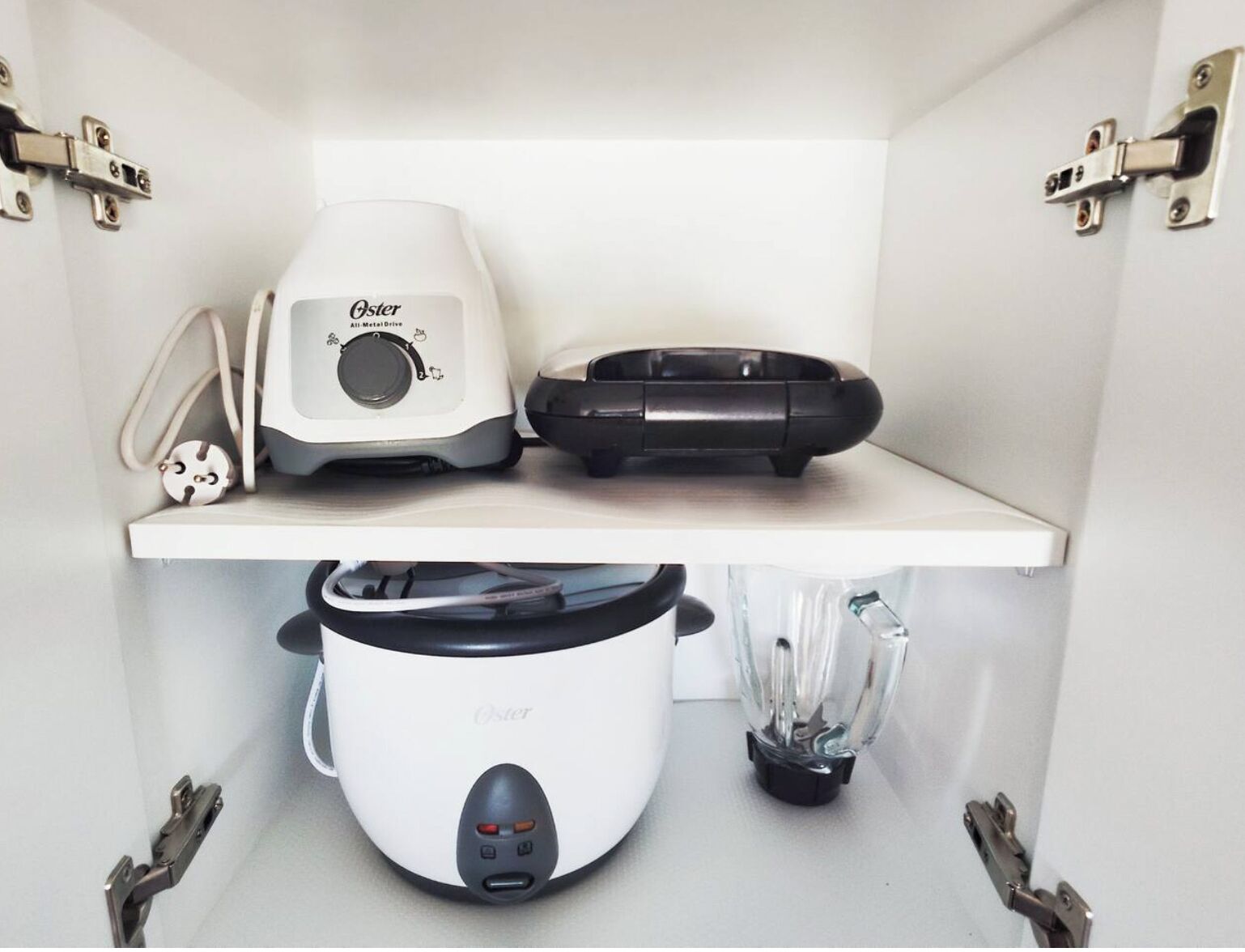 A kitchen with a white countertop, a white Oster All-Metal Drive blender, a black Oster food processor, and a white Oster slow cooker.