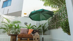 A cozy outdoor seating area with a green umbrella, a wooden bench, and a variety of plants. - Modern 3-bedroom townhome with a pool, AC and Wi-Fi in vibrant East Legon (Accra)