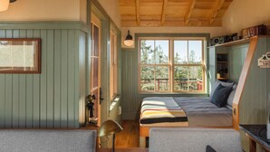L’intérieur d’un chalet accueillant, avec un lit, deux fauteuils, un bureau, une lampe et une fenêtre donnant sur une forêt.