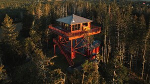 Une structure en bois en forme de tour, dotée d’un balcon, et entourée d’une forêt.