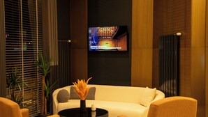 A modern lobby with a sofa, chairs, a coffee table, and a TV displaying a program. - Rest By Dedeman Elbistan (Elbistan)