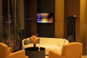 Um lobby moderno com um sofá, cadeiras, uma mesa de centro e uma TV exibindo um programa.