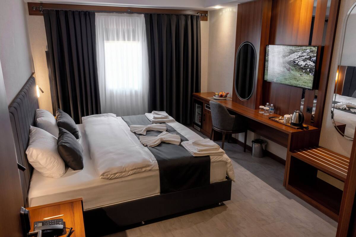 A hotel room with a bed, desk, TV, and a small seating area.