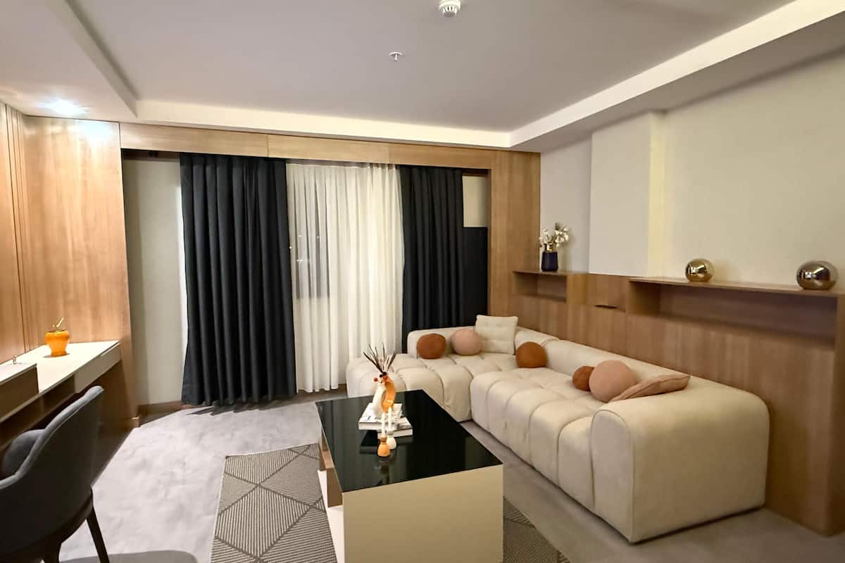 A modern hotel room with a sofa, a coffee table, a TV, and a desk.