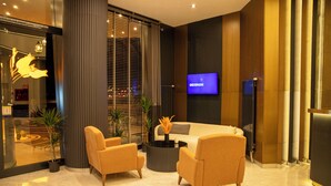 A modern lobby with a sofa, two armchairs, a coffee table, and a TV screen displaying 'DEDEMAN'. - Rest By Dedeman Elbistan (Elbistan)