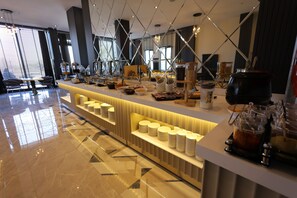 Zona de bufé con diversos alimentos y bebidas, un área de estar con sillas y una decoración interior moderna.