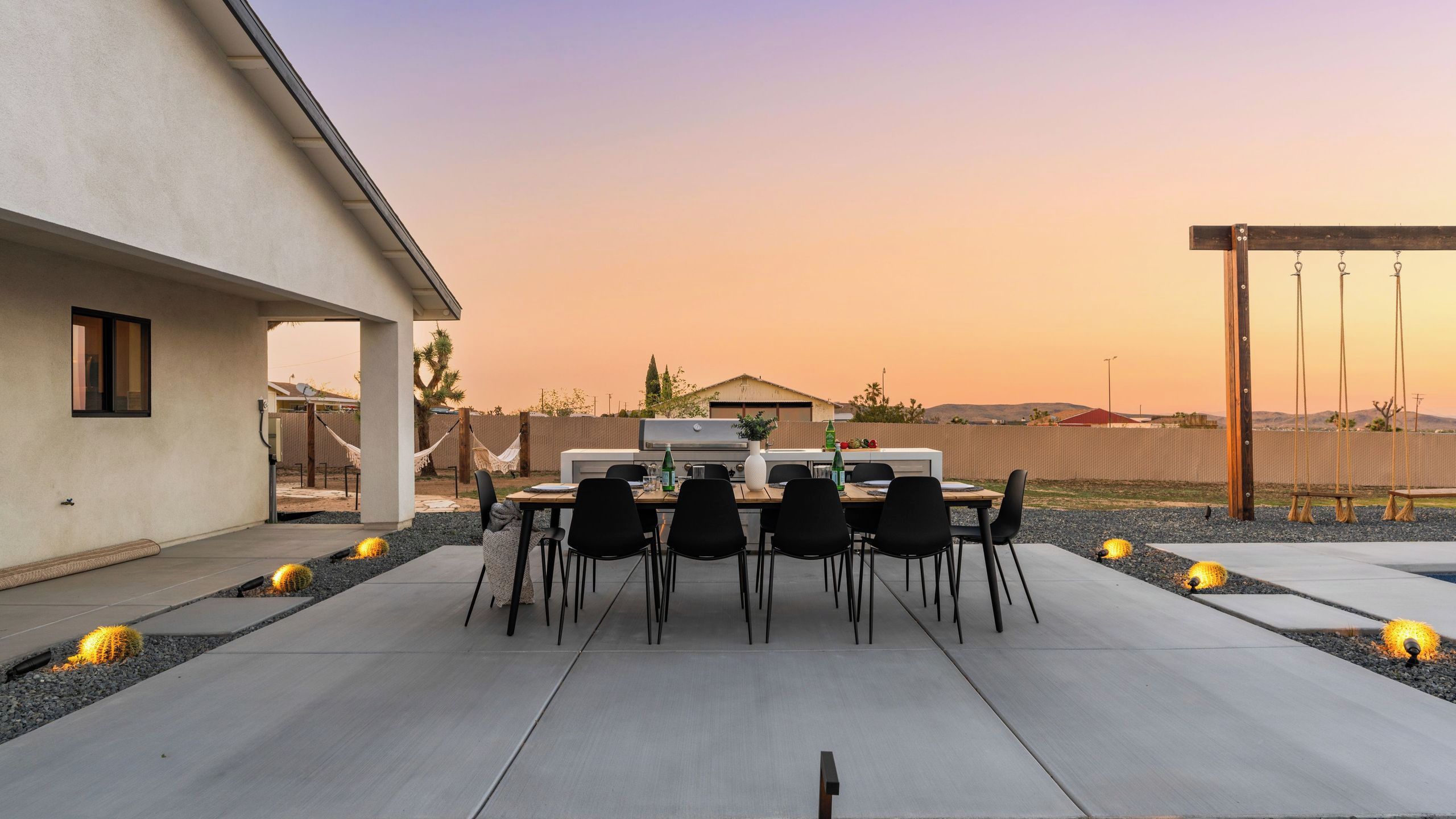 A patio with a table and chairs, a grill, and a swing set.