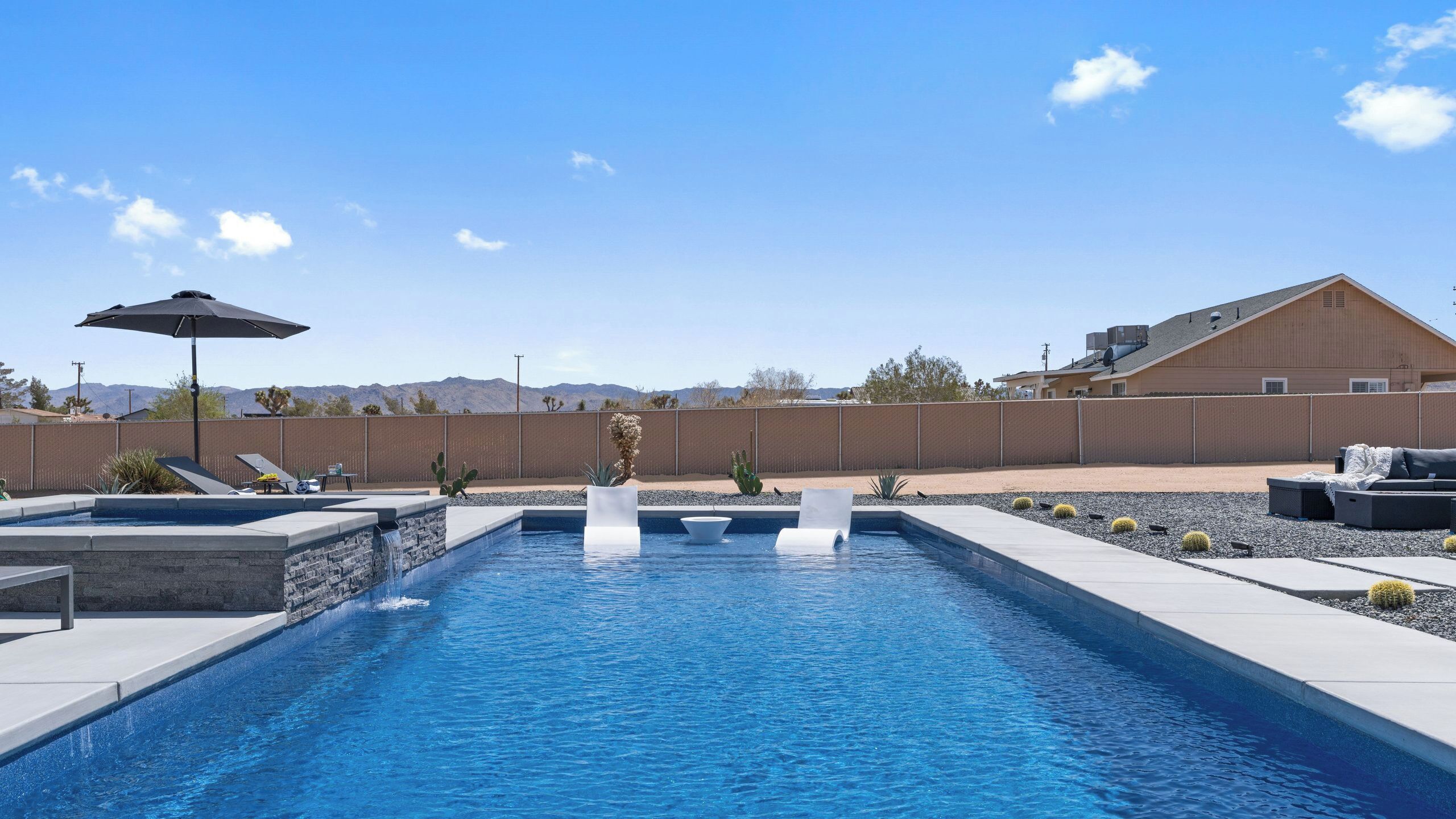 A swimming pool with a waterfall feature, lounge chairs, and a view of mountains.