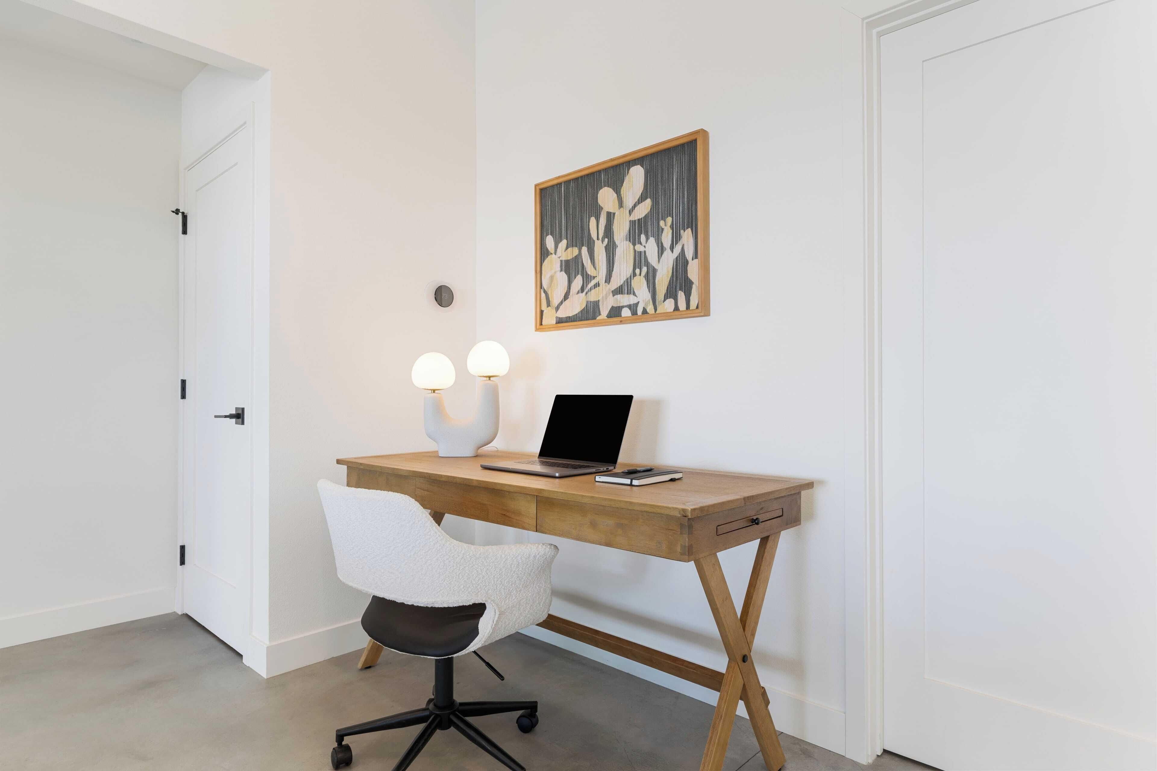 A modern office space with a wooden desk, a white office chair, a laptop, and a wall-mounted light fixture.