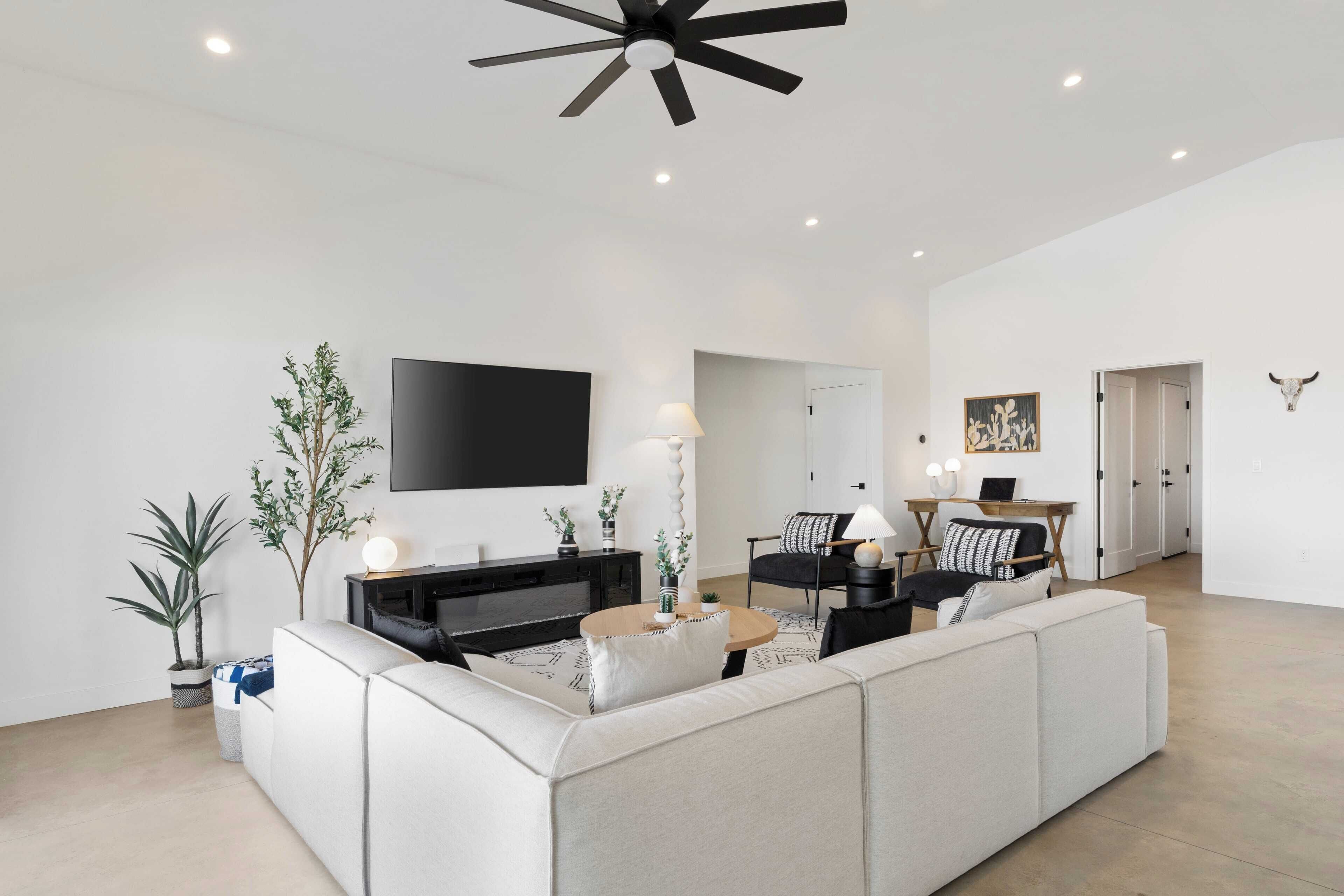 A modern living room with a large L-shaped sectional sofa, a flat-screen TV mounted on the wall, and a ceiling fan.