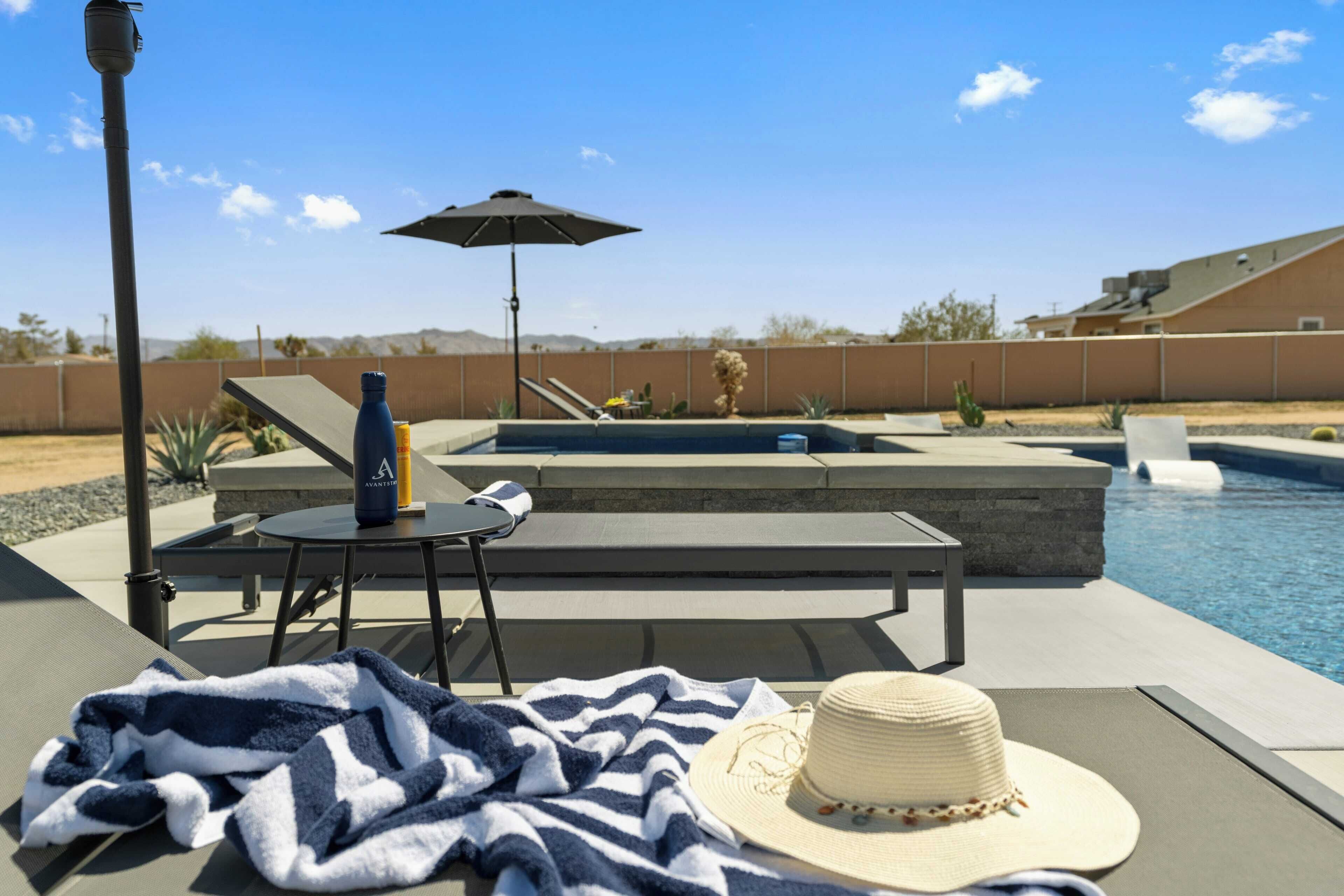 A poolside area with lounge chairs, a table, a bottle, and a hat.