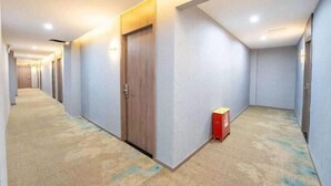A corridor with a carpeted floor, a wooden door, and a red box against the wall. - Home Inn Baiyun Hotel (Huai'an Railway Station Mandu Plaza) (Huai'an)