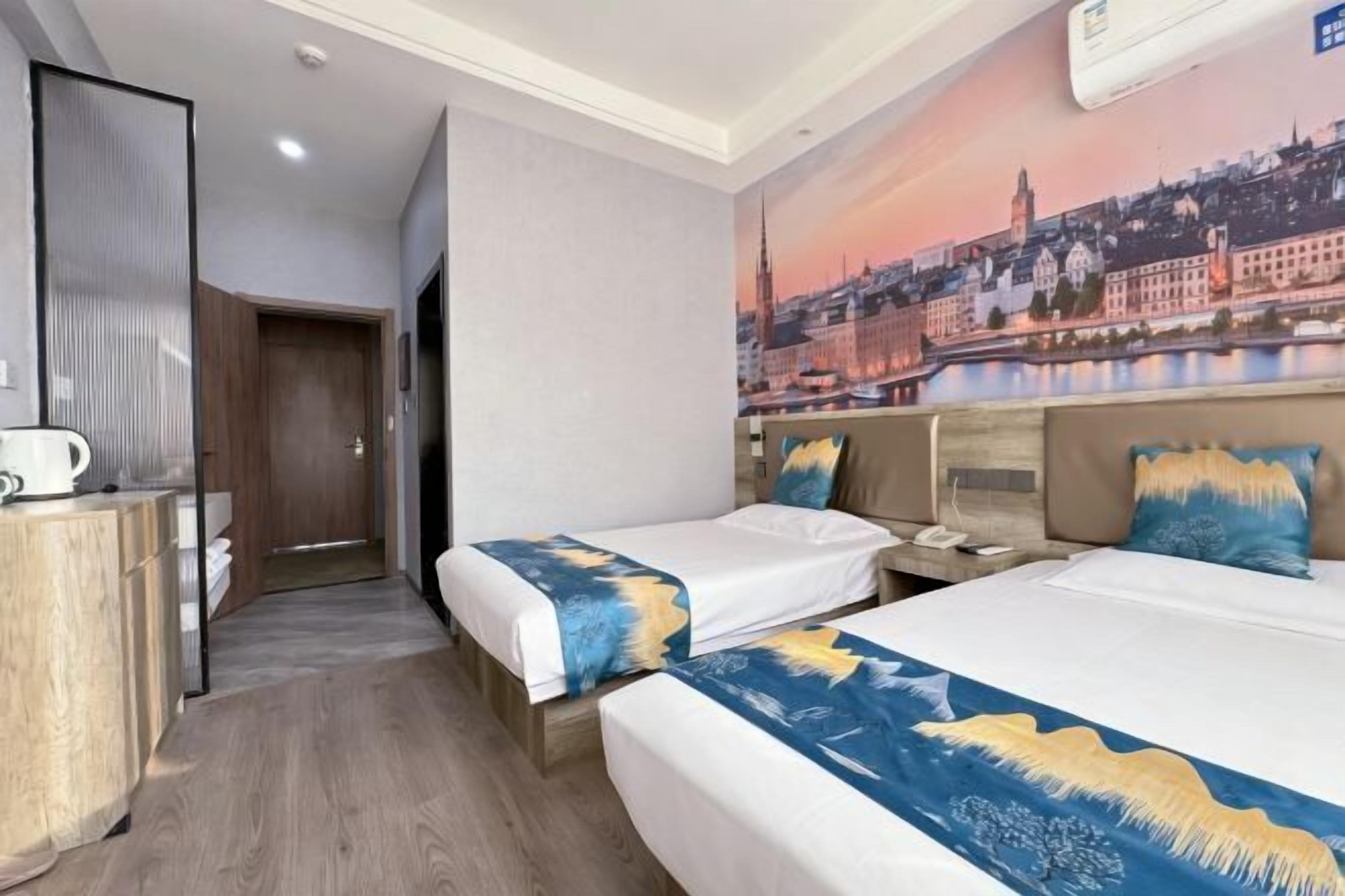 A hotel room with two beds, a cityscape mural on the wall, and a wooden wardrobe.