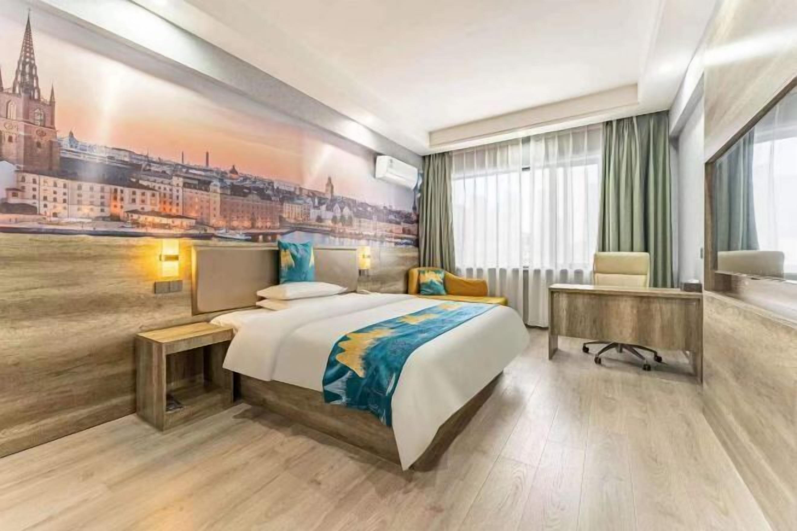 Quarto de hotel com uma cama, uma escrivaninha, uma cadeira, uma janela com cortinas e um mural na parede.