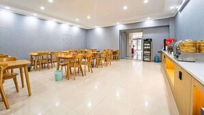 A spacious dining area with wooden tables and chairs, a counter with food items, and a door leading to another room. - Home Inn Baiyun Hotel (Huai'an Railway Station Mandu Plaza) (Huai'an)