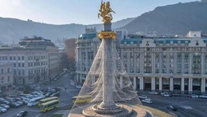 Un grand monument circulaire surmonté d’une statue dorée, entouré d’un espace paysager agrémenté d’une fontaine au centre.