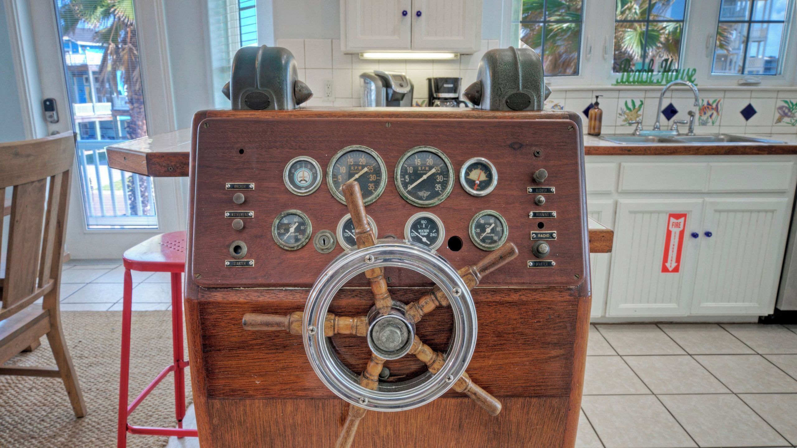 Une vieille radio en bois, dotée de boutons et d’une molette, est posée dans une cuisine aux meubles blancs, près d’une fenêtre.