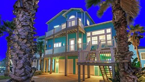 A two-story house with a balcony, a garage, and a palm tree in the foreground. - Point Break by Avantstay Ocean View Escape Game Garage Golf Cart Zone (Port Aransas)