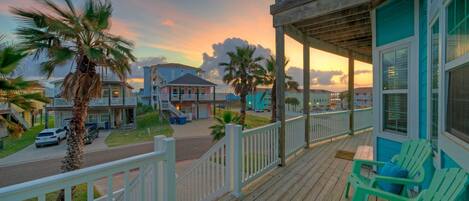 A wooden deck with a railing, a covered area with chairs, and a view of the street and buildings in the background.