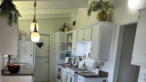Ett modernt kök med vita skåp, ett matbord i glas och vita stolar.