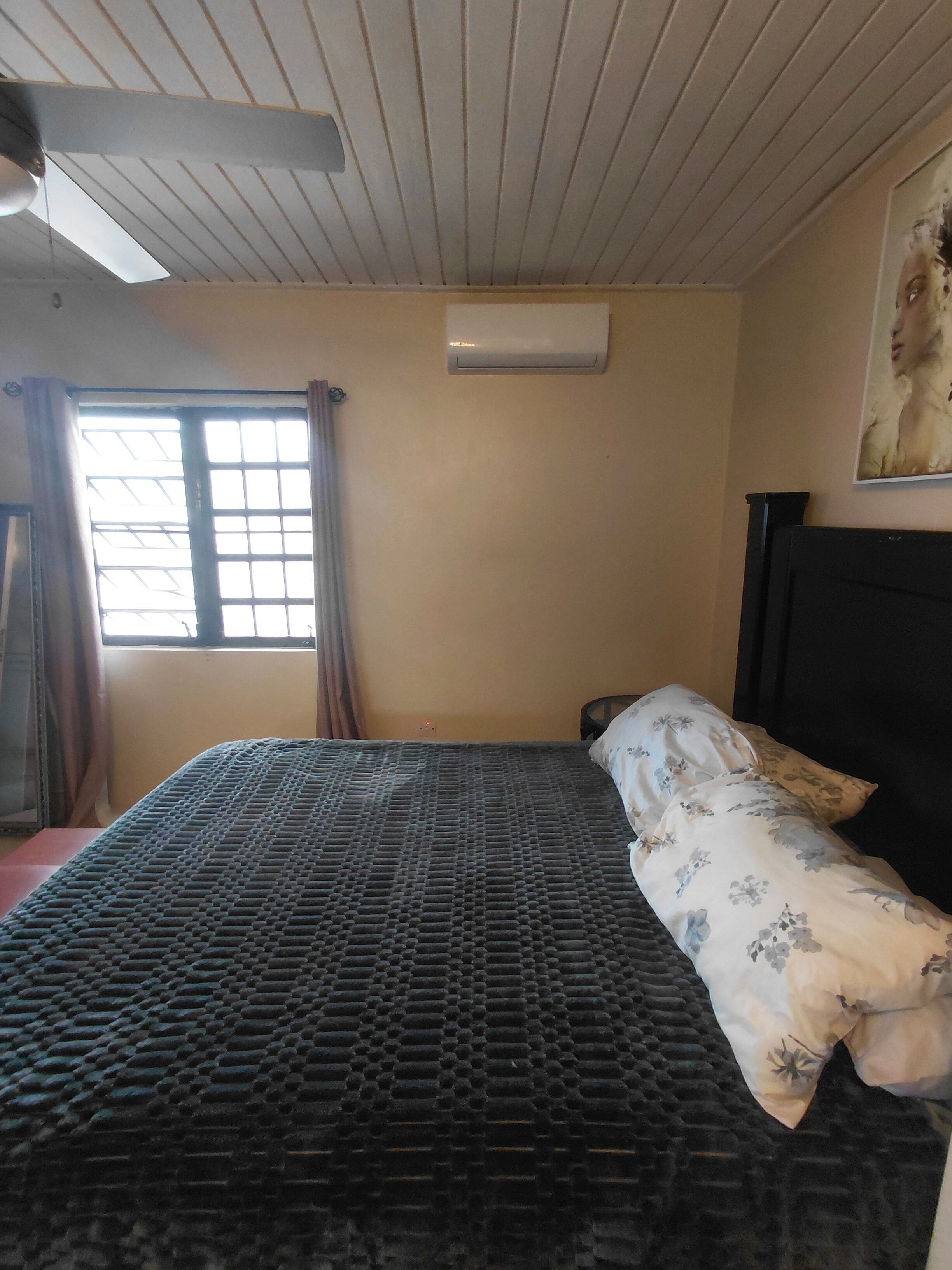 Ein Zimmer mit einem Bett, einer Klimaanlage, einem Fenster mit Vorhängen und einem Deckenventilator.